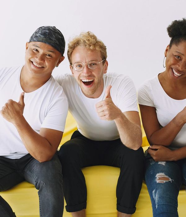 Diverse group of people smiling and sitting on yoga mats in a bright studio.